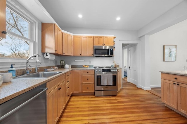 kitchen with stainless steel appliances, light stone countertops, sink, and light hardwood / wood-style flooring