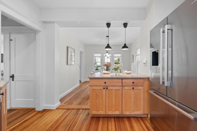 kitchen with light stone counters, decorative light fixtures, light brown cabinets, high quality fridge, and light hardwood / wood-style floors