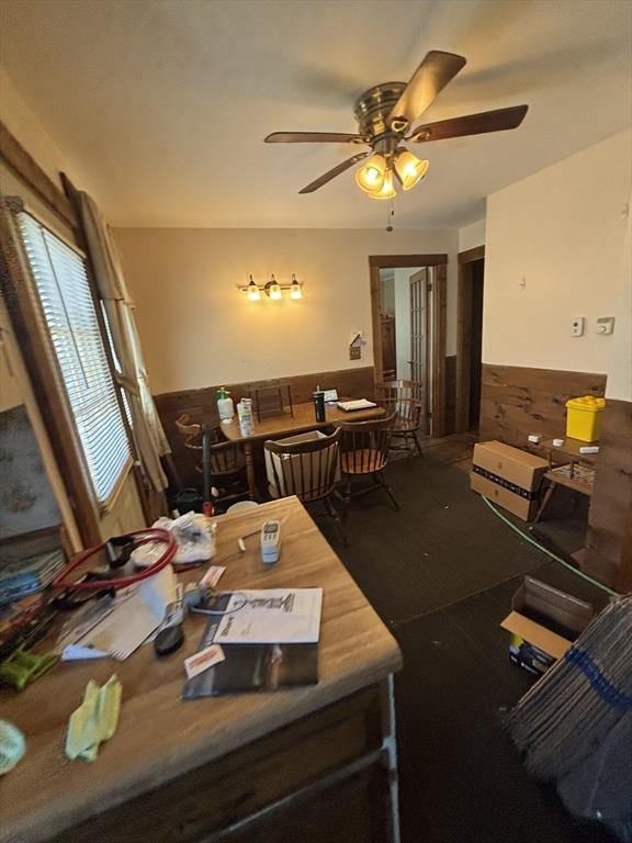 dining area with a ceiling fan and a wainscoted wall