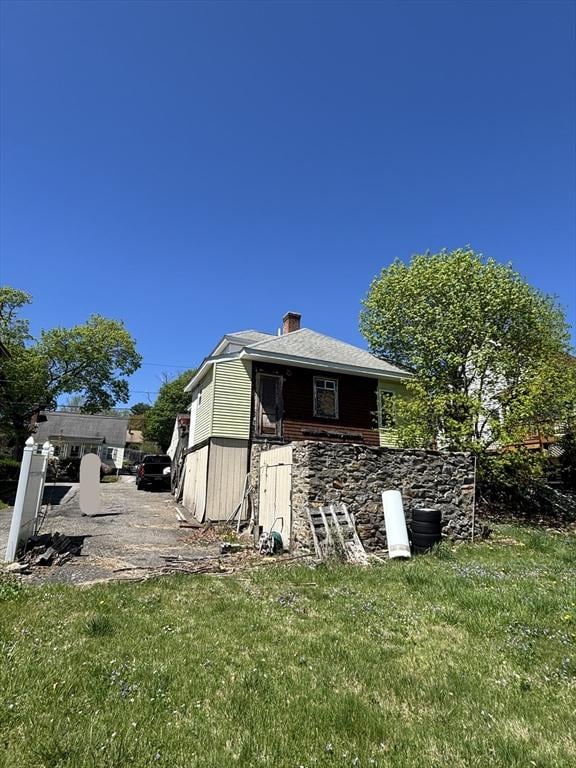 back of house with a chimney and a lawn