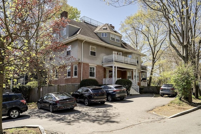 view of front facade featuring fence, a balcony, and a chimney