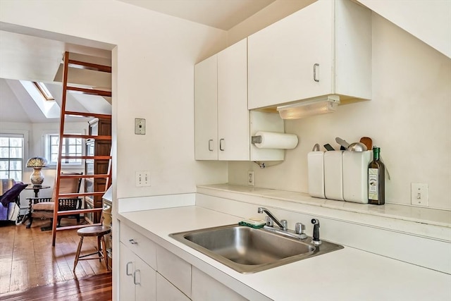 kitchen featuring a sink, light countertops, lofted ceiling with skylight, white cabinetry, and dark wood-type flooring