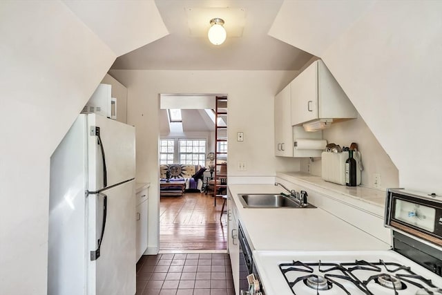 kitchen featuring freestanding refrigerator, light countertops, dark tile patterned flooring, range with gas cooktop, and a sink