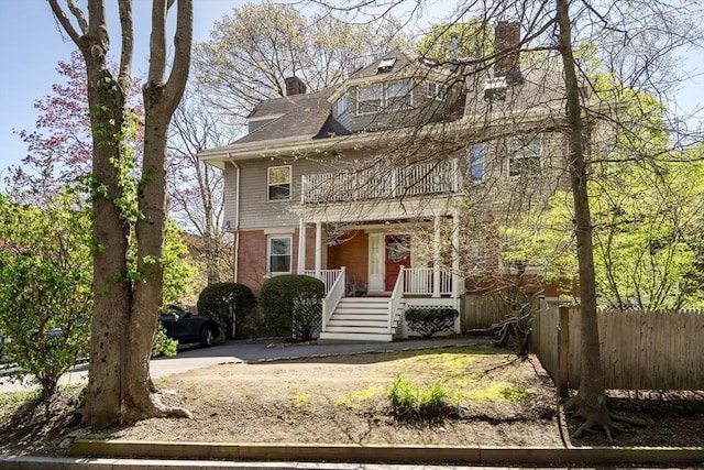 american foursquare style home with a porch, brick siding, fence, and a chimney