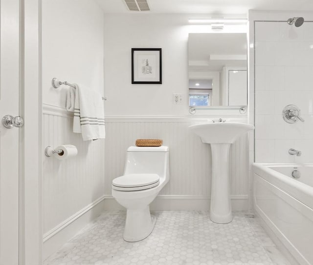 full bathroom with visible vents, bathing tub / shower combination, toilet, tile patterned floors, and a wainscoted wall