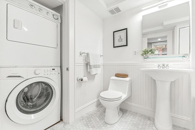 bathroom featuring visible vents, wainscoting, toilet, a sink, and stacked washer / drying machine