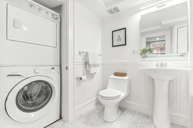 bathroom with visible vents, stacked washing maching and dryer, a wainscoted wall, a sink, and toilet