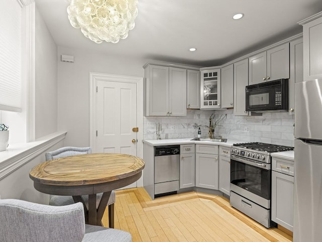 kitchen featuring an inviting chandelier, decorative backsplash, gray cabinets, a sink, and stainless steel appliances