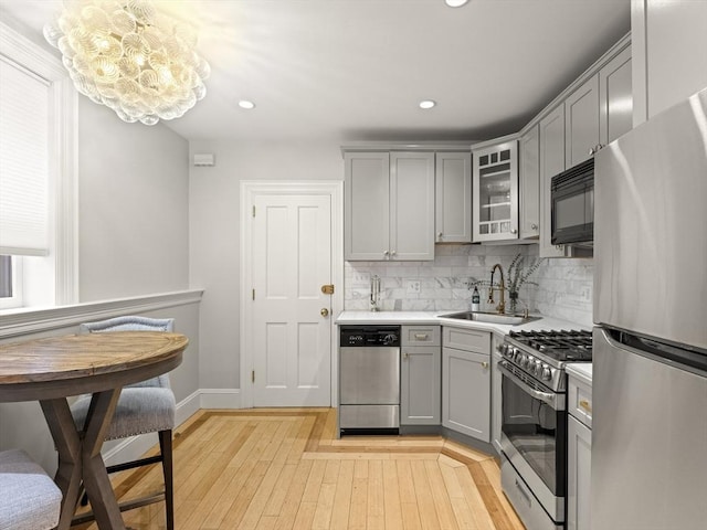 kitchen featuring appliances with stainless steel finishes, a sink, a chandelier, gray cabinets, and light wood-style flooring