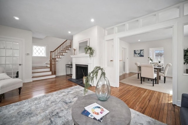 living area featuring stairs, recessed lighting, a fireplace with raised hearth, and wood-type flooring