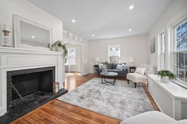 living area featuring hardwood / wood-style flooring, recessed lighting, a fireplace with raised hearth, and baseboards