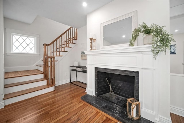 living room with stairway, wood finished floors, baseboards, and a fireplace with raised hearth