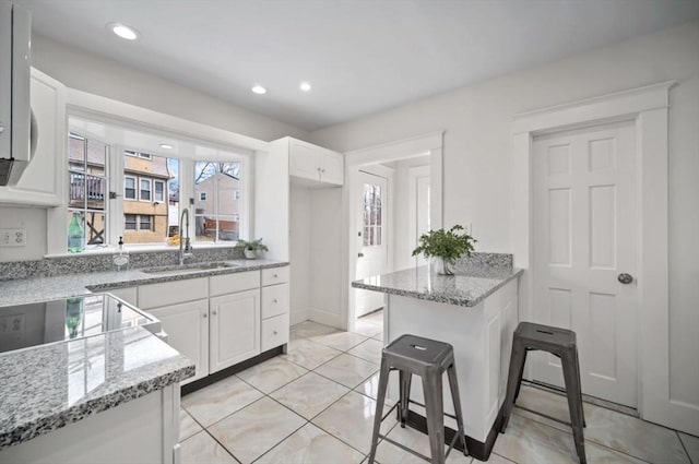 kitchen featuring a sink, white cabinetry, recessed lighting, range, and light stone countertops