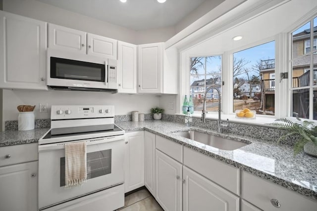 kitchen featuring white cabinets, white appliances, light stone countertops, and a sink