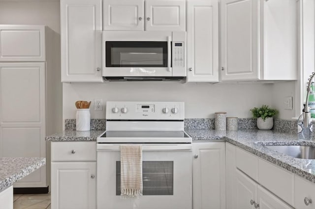 kitchen featuring light stone counters, white appliances, white cabinets, and a sink