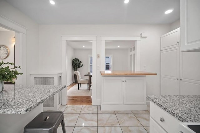 kitchen featuring white cabinets, recessed lighting, light stone countertops, and baseboards