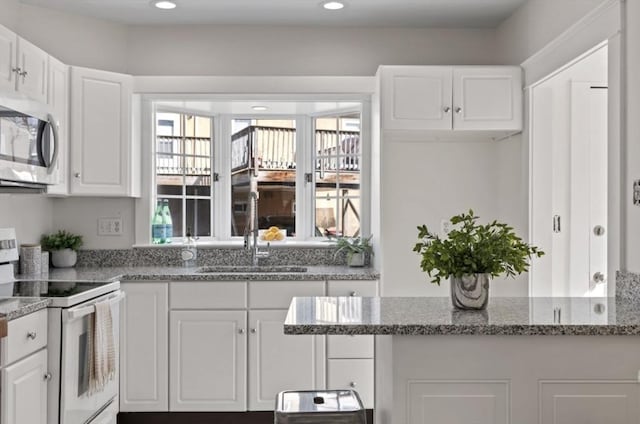 kitchen with stainless steel microwave, plenty of natural light, white cabinetry, white electric range, and a sink