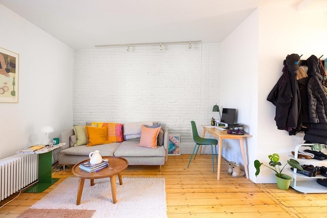 living area featuring hardwood / wood-style floors, brick wall, radiator heating unit, and track lighting