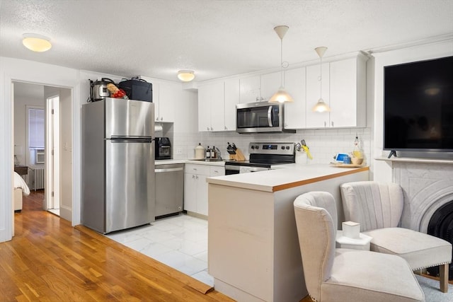 kitchen featuring decorative light fixtures, kitchen peninsula, white cabinets, stainless steel appliances, and backsplash