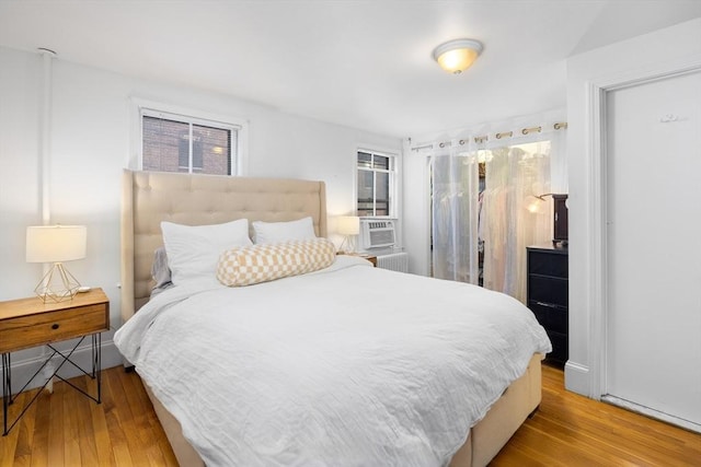 bedroom with cooling unit, radiator heating unit, and wood-type flooring