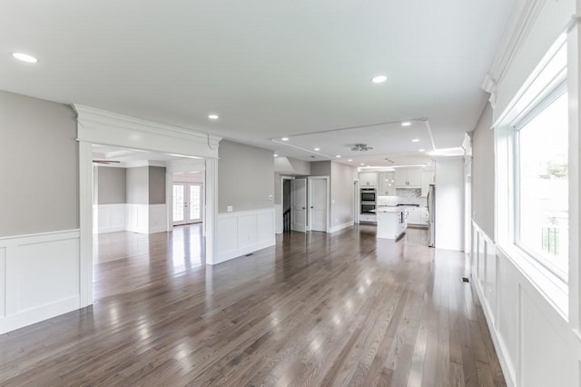 unfurnished living room featuring dark wood-style floors, recessed lighting, wainscoting, a decorative wall, and crown molding