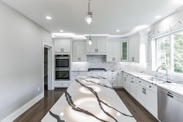 kitchen with pendant lighting, a sink, dark wood finished floors, appliances with stainless steel finishes, and decorative backsplash