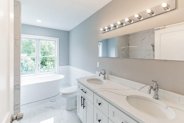 bathroom featuring marble finish floor, a freestanding bath, toilet, and a sink