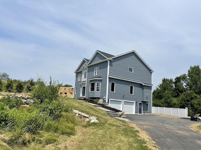 view of property exterior featuring driveway, a garage, and fence