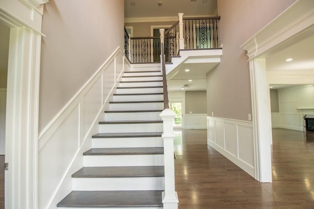 stairway featuring wood finished floors, a high ceiling, wainscoting, crown molding, and a decorative wall