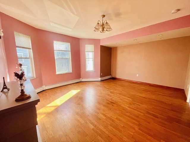 spare room with hardwood / wood-style flooring, an inviting chandelier, a wealth of natural light, and baseboard heating