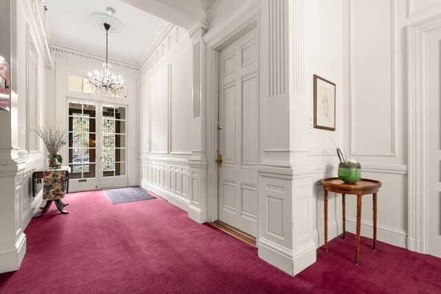 interior space featuring ornamental molding, a decorative wall, dark carpet, and a chandelier