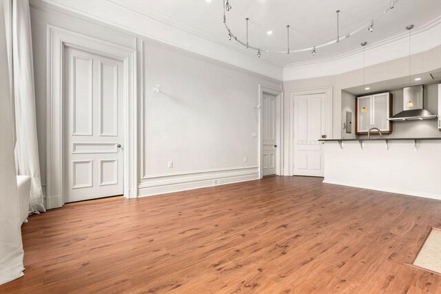 unfurnished living room featuring rail lighting, ornamental molding, wood finished floors, and electric panel