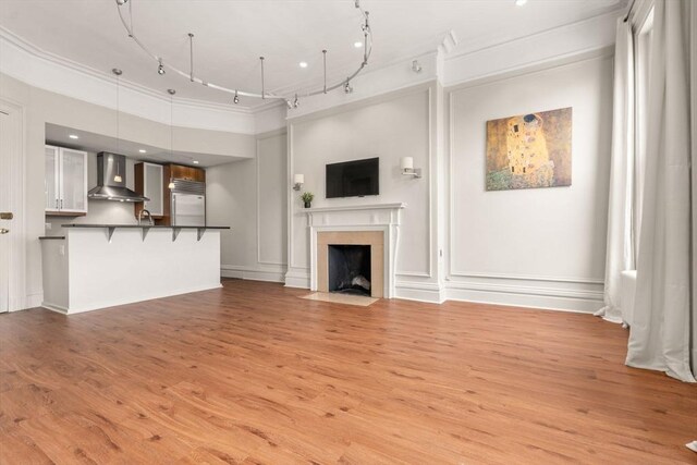 unfurnished living room featuring light wood-style floors, track lighting, and ornamental molding