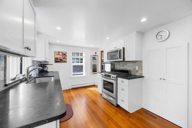 34 Kenwood Rd, Bourne, MA 02559 - kitchen featuring stainless steel appliances, a baseboard heating unit, dark countertops, light wood finished floors, and decorative backsplash
