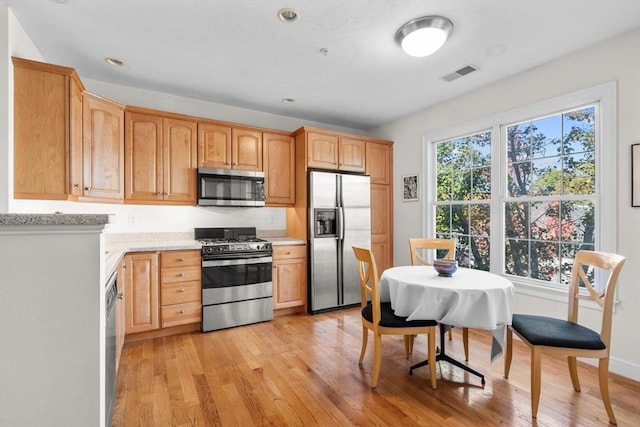 kitchen with light wood-type flooring, light brown cabinets, appliances with stainless steel finishes, and light stone counters