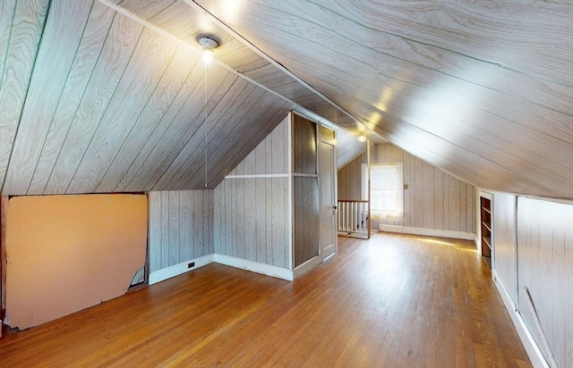 additional living space featuring hardwood / wood-style flooring, vaulted ceiling, and wooden walls