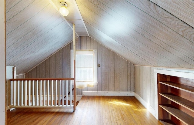 additional living space with wood walls, lofted ceiling, and light wood-type flooring