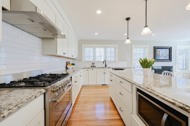 kitchen featuring wall chimney exhaust hood, gas range, white cabinetry, light stone counters, and decorative light fixtures