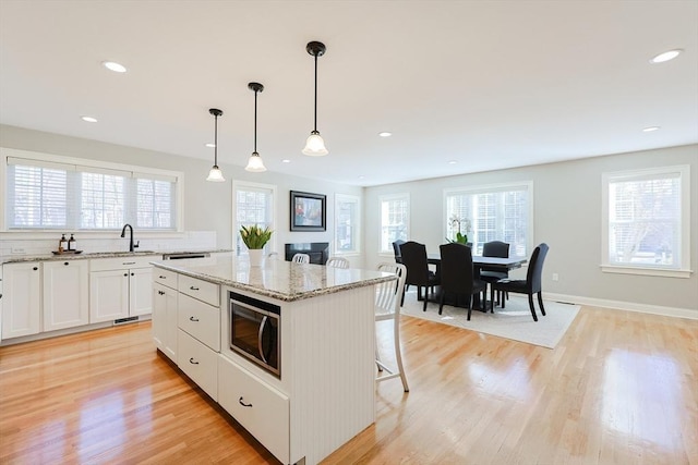 kitchen featuring a kitchen bar, a center island, light wood-type flooring, pendant lighting, and white cabinets