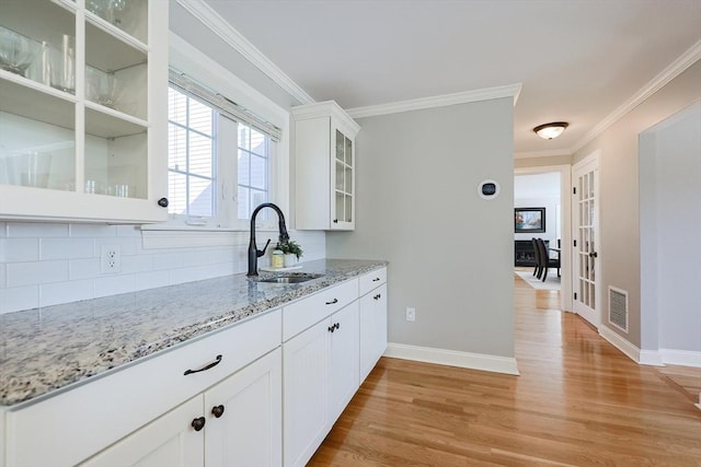 kitchen with sink, light hardwood / wood-style flooring, ornamental molding, light stone countertops, and white cabinets