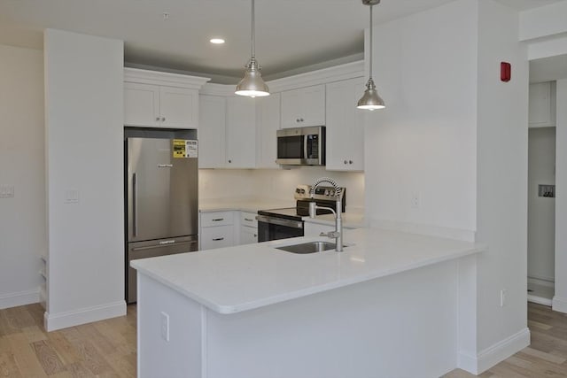 kitchen with appliances with stainless steel finishes, white cabinets, hanging light fixtures, kitchen peninsula, and light hardwood / wood-style flooring