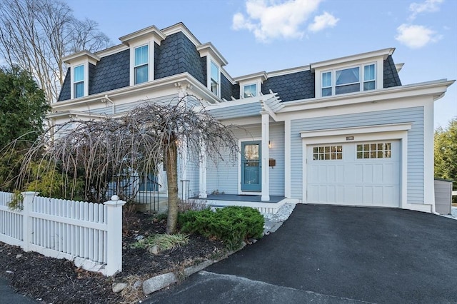 second empire-style home with covered porch, mansard roof, driveway, and fence