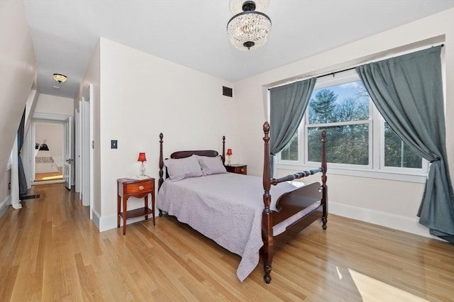 bedroom with an inviting chandelier, visible vents, baseboards, and light wood-type flooring