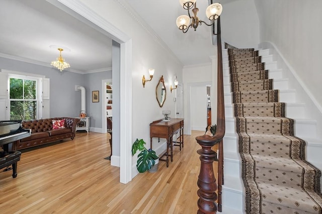 foyer entrance featuring stairway, baseboards, light wood finished floors, crown molding, and a chandelier