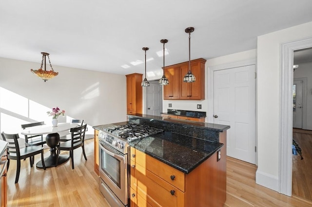 kitchen with a kitchen island, gas stove, dark stone counters, brown cabinetry, and light wood finished floors