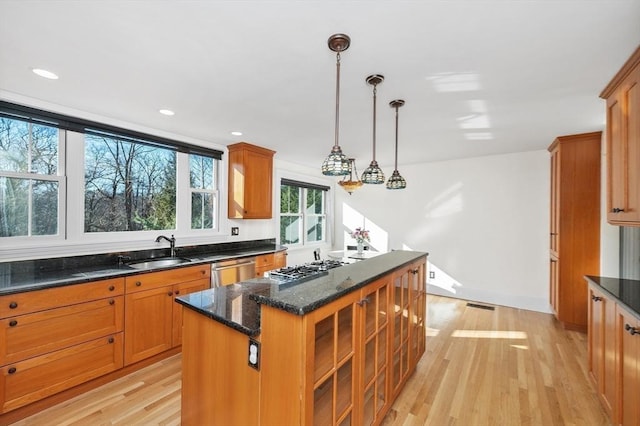 kitchen with brown cabinetry, appliances with stainless steel finishes, light wood-style floors, and a sink