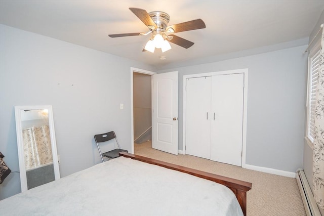 bedroom with a closet, light colored carpet, baseboard heating, ceiling fan, and baseboards