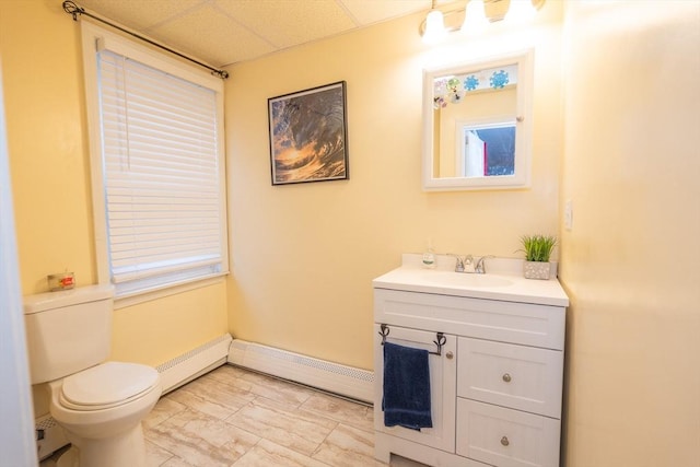 half bathroom with toilet, a baseboard radiator, vanity, a paneled ceiling, and a baseboard heating unit