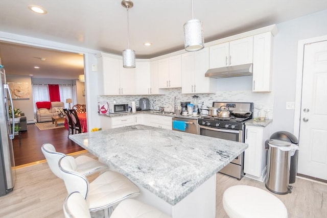 kitchen featuring a kitchen island, appliances with stainless steel finishes, hanging light fixtures, under cabinet range hood, and white cabinetry