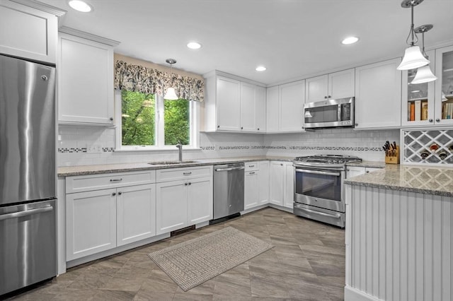 kitchen featuring white cabinets, light stone counters, glass insert cabinets, stainless steel appliances, and a sink